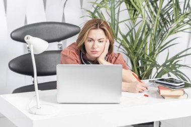 Bir kadın dizüstü bilgisayarıyla çalışıyor ve stresli görünüyor.
