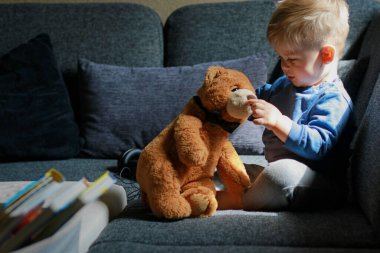 Küçük çocuk kanepede oynuyor ve oyuncak ayıya sarılıyor. Yüksek kalite fotoğraf