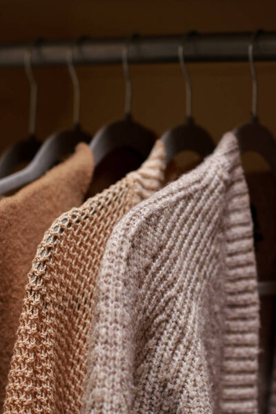 close up of pastel warm knitted cardigan sweater hanging in the closet. Cozy fall and winter wardrobe. High quality photo