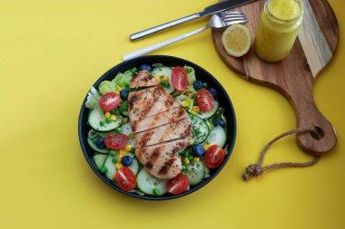 Siyah tabakta ızgara tavuk salatası, ballı hardal sosu, fotokopi alanı olan sarı arka plan. Yüksek kalite fotoğraf