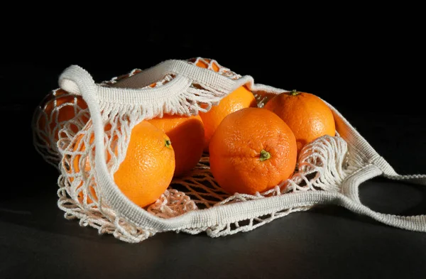 fresh oranges in a eco organic cotton mesh grocery bag, grey table and dark background .