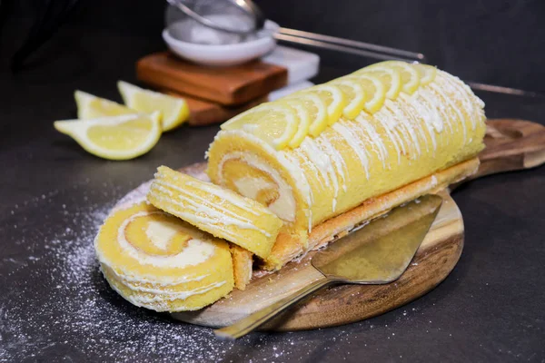 delicious vanilla cake roll with lemon butter cream inside and lemons on top, dark grey marble table and copy space