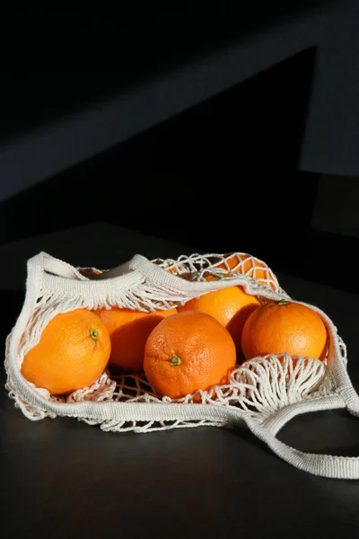 fresh oranges in a eco organic cotton mesh grocery bag, grey table and dark background .