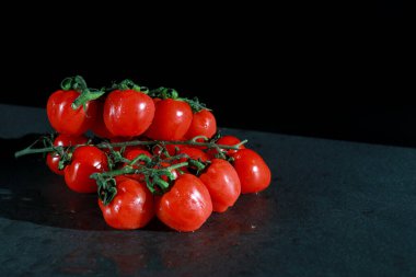 bunch of fresh cherry tomatoes with green stems isolated on dark grey marble table with copy space 