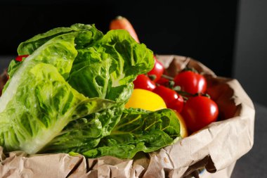 Eko kağıt torbada taze romana marulu ve diğer sebzelerle birlikte koyu arkaplan. Temiz vejetaryen yeme kavramı. 