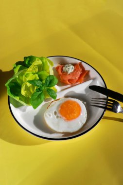 Kızarmış yumurta, yeşil salata ve sarı arka planda füme somon ile sağlıklı ketojenik kahvaltı.