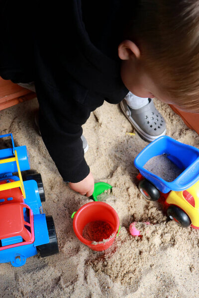 upper view of a toddler playing in the sand with toys. 