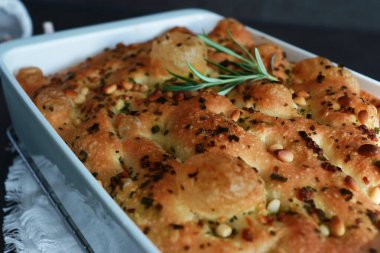 İtalyan geleneksel sarımsaklı ve biberiyeli Focaccia ekmeği beyaz fırın tavasında güneş ışığıyla birlikte gri masada. 