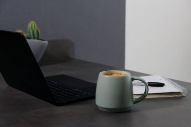 Yeşil kahve fincanını, not defterini ve gri mermer masadaki siyah dizüstü bilgisayarı kapat.