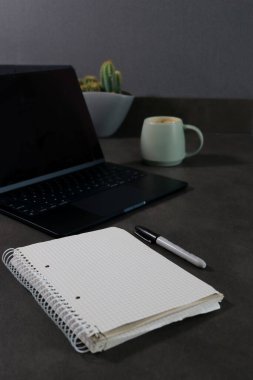 Boş dizüstü bilgisayarı ve gri mermer masada yeşil kahve fincanı olan boş defteri kapat.