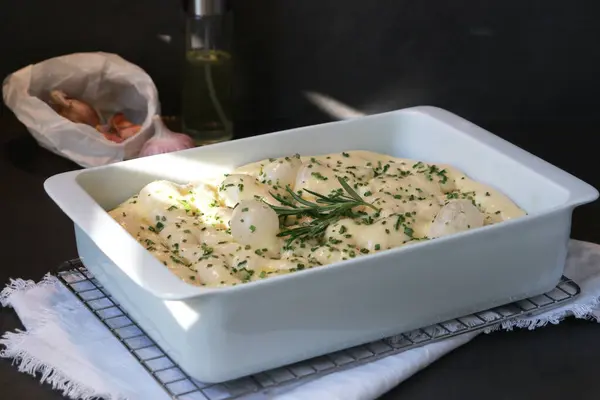 stock image Raw focaccia dough in white baking dish with garlic rosemary, dark grey table