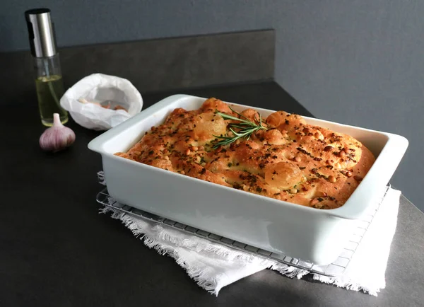 stock image Italian traditional garlic rosemary focaccia bread in white baking pan on grey table with sunlight 