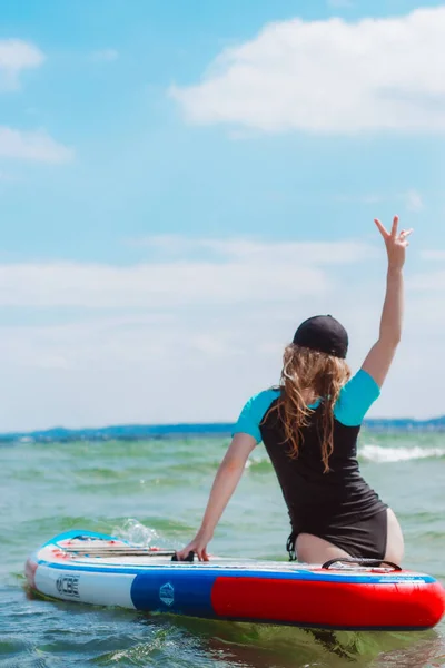 ブロンドの髪に乗って若い女性は海の中でパドルボードを立っています 自然界の健康と健康的な生活 — ストック写真