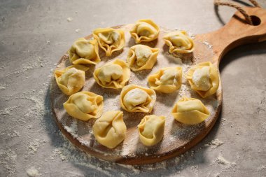 Tahta tabakta çiğ ravioli tortellini, unlu gri masa.