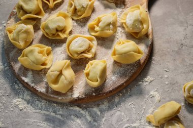 Tahta tabakta çiğ ravioli tortellini, unlu gri masa.