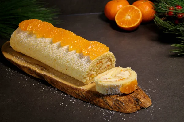 Delicious tangerine cake roll with vanilla buttercream filling on wooden plate, grey table, holiday winter dessert