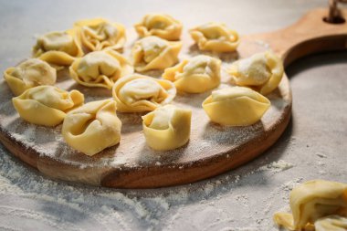 Çiğ geleneksel ravioli tortellini 'sini ahşap tabakta, unlu gri masa.