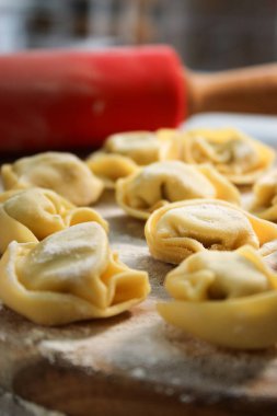 Çiğ geleneksel ravioli tortellini 'sini ahşap tabakta, unlu gri masa.