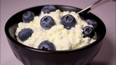 Süzme peyniri, mavi arka planda siyah kasede taze yaban mersini ve protein tatlısı ile kapatın.. 