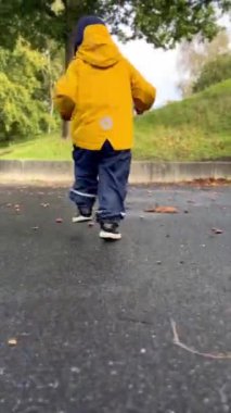 Sarı yağmurluklu küçük çocuk oyun parkında koşuyor, sonbahar havası erken.