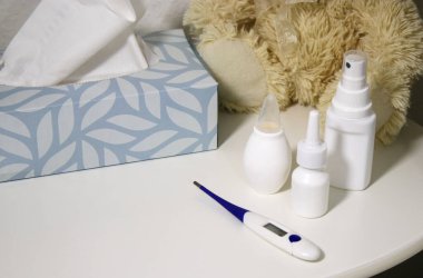 Fil ilacı şişeleri ve beyaz masanın üzerinde bir termometre ve çocuk odasında bir oyuncak ayı. 