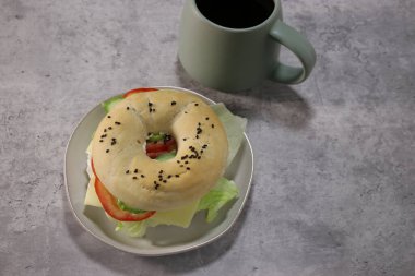 Vejetaryen peynirli lezzetli simit ve tabakta taze sebzeler, gri masa arkaplanı. 