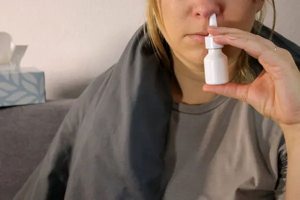 Close up of sick woman with red nose using a nose spray, blurry background with copy space
