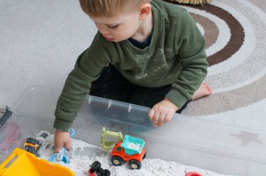 Evde plastik bir kutuda beyaz ev yapımı kinetik kumla oynayan küçük bir çocuk, güzel motor beceriler kavramının gelişimi 
