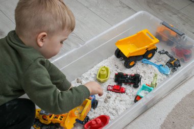 Evde plastik bir kutuda beyaz ev yapımı kinetik kumla oynayan küçük bir çocuk, güzel motor beceriler kavramının gelişimi 