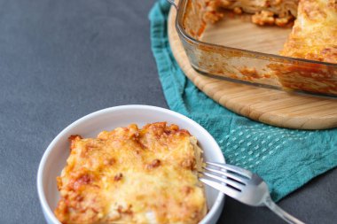 Ev yapımı vejetaryen lazanya, soya eti ve vegan peyniri beyaz tabakta, gri mutfak masasında. 
