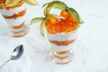 Beyaz mermer masanın üzerinde cam bir kavanozda protein yoğurdu ve bitki özü içeren katmanlı tatlı manzarası. 