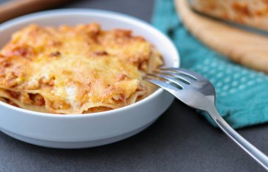 Ev yapımı vejetaryen lazanya, soya eti ve vegan peyniri beyaz tabakta, gri mutfak masasında. 