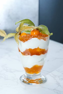 Bir kavanoz katmanlı tatlı protein yoğurdu ve beyaz mermer masada bitki özü. 