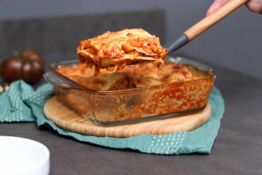 El ele tutuşmuş ev yapımı soya vegan lazanya spatulada, gri mermer mutfak masasında