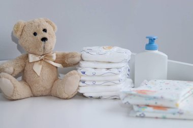 Bir yığın bebek bezi, tulum, oyuncak ayı ve bebek malzemeleri beyaz soyunma masasında, hemşire odasında. 