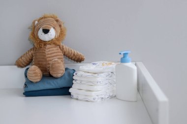 Bir yığın bebek bezi, mavi tulum, peluş aslan ve bebek malzemeleri.