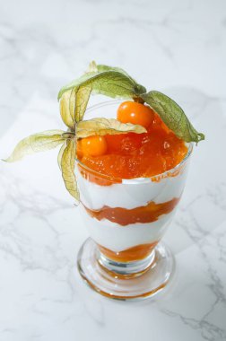 Bir kavanoz katmanlı tatlı protein yoğurdu ve beyaz mermer masada bitki özü. 