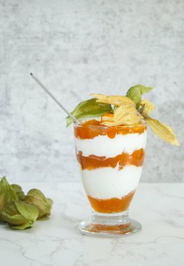 Bir kavanoz katmanlı tatlı protein yoğurdu ve beyaz mermer masada bitki özü. 