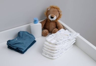 Bir yığın bebek bezi, mavi tulum, peluş aslan ve bebek malzemeleri.