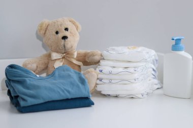 Bir yığın bebek bezi, tulum, oyuncak ayı ve bebek malzemeleri beyaz soyunma masasında, hemşire odasında. 