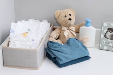 Bir yığın bebek bezi, tulum, oyuncak ayı ve bebek malzemeleri beyaz soyunma masasında, hemşire odasında. 