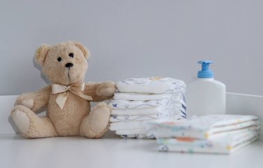 Bir yığın bebek bezi, tulum, oyuncak ayı ve bebek malzemeleri beyaz soyunma masasında, hemşire odasında. 