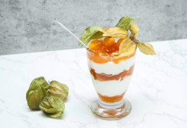 Bir kavanoz katmanlı tatlı protein yoğurdu ve beyaz mermer masada bitki özü. 