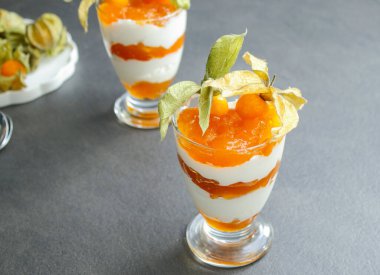 Gri masadaki cam bir kavanozda protein yoğurdu ve bitki özü ile katmanlanmış tatlı. 