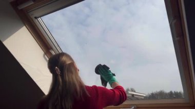 Gündüz vakti evde Velux penceresini temizleyen genç bir kadın. Arka plan 