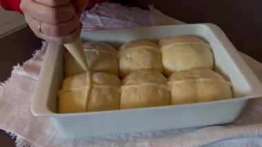 Kadınların elleri tavada çiğ haç çörekleri üzerinde kuyruk oluşturuyor.