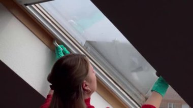 Gündüz vakti evde Velux penceresini temizleyen genç bir kadın. Arka plan 