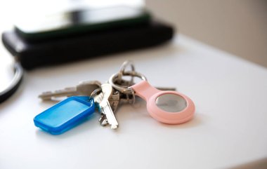 Anahtarları beyaz masada elmalı bir AirTag ile kapat, akıllı telefon ve cüzdan ile bulanık arkaplan 