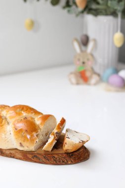 Cutted easter loaf bread on wooden plate on white table, blurry background with easter decoration. clipart