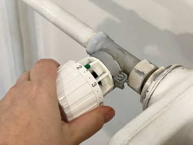 Orta pozisyondaki termostat radyatörünü çeviren bir ele yaklaş. Soğuk mevsim konseptinde evlerin ısıtılması